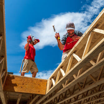 two men, one hammering a nail, and one operating a circular saw