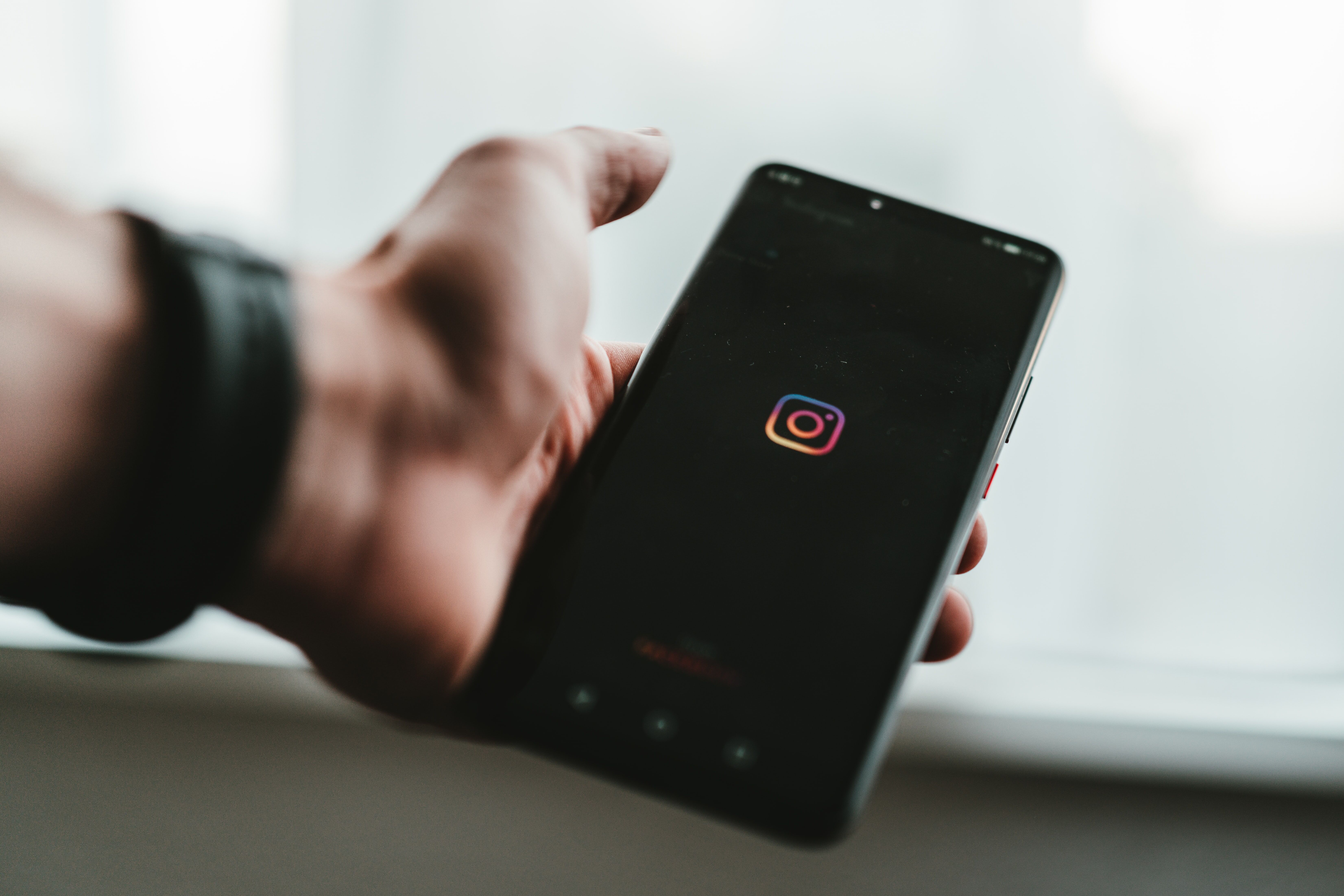 Person holding a black phone with the Instagram logo on the screen.