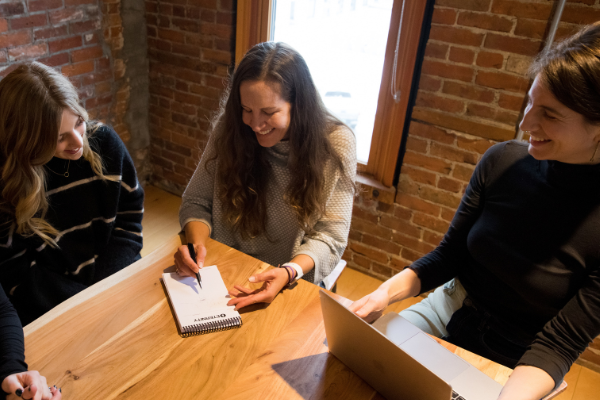 A group of 4 marketers sitting around a table with a laptop and pad of paper having a meeting