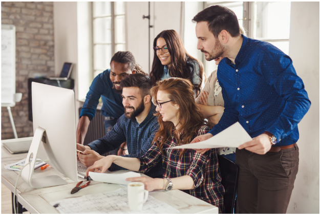 group of happy people gathered around and looking at a computer monitor